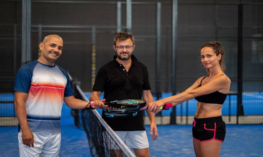 Portrait of smiling sportsman's posing indoor on padel court with rackets and balls, 